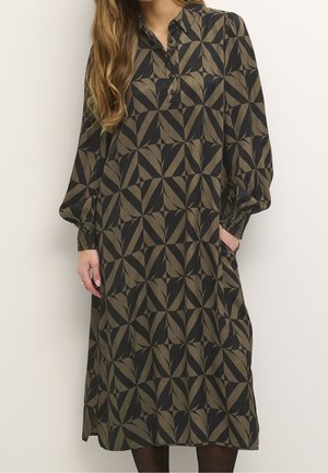 Robe à manches longues et col en vert foncé avec des motifs géométriques de feuilles. Comprend des boutons, des manches légèrement bouffantes et des poches. Texture du tissu lisse.