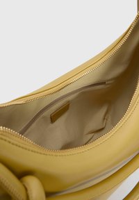 Geel leren handtas met een gladde textuur, voorzien van een gouden rits en een binnenzak met rits. Eenvoudig, functioneel ontwerp.