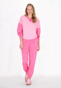 Felpa rosa con maniche a contrasto e pantaloni della tuta rosa coordinati. Tessuto morbido, vestibilità rilassata e polsini elasticizzati. Calzature di una tonalità più chiara di rosa.