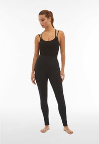 Body nero senza maniche con spalline sottili abbinato a leggings neri a vita alta. Texture liscia, design aderente, senza motivi visibili.