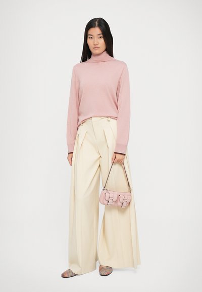 Maglione a collo alto rosa chiaro, pantaloni a gamba larga crema e una piccola borsa rosa. Le calzature presentano un motivo a strisce multicolori.