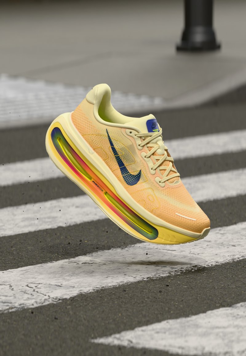 Αθλητικό παπούτσι Nike με επάνω μέρος από ανοιχτό κίτρινο διχτυωτό υλικό, μπλε λεπτομέρειες και πολύχρωμη σόλα με αερόσολα. Ριγέ επιφάνεια από κάτω.