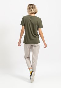 Olijfgroene katoenen t-shirt met een ontspannen pasvorm, korte mouwen en een ronde halslijn. Gecombineerd met lichtbeige broeken en zwarte sneakers.