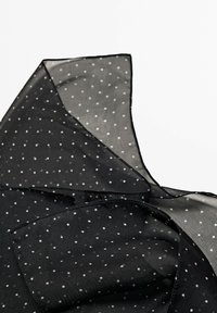 Tessuto nero trasparente con pois bianchi, caratterizzato da un design fluido e una texture morbida. I bordi presentano un delicato dettaglio di cucitura nera.
