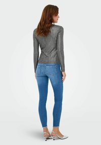 Slim-fit, gestructureerde grijze long-sleeve top met verticale strepen, gecombineerd met blauwe skinny jeans en zilveren sandalen met hakken, gezien van achteren.