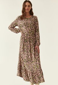 Langärmliges Blumenkleid mit rundem Ausschnitt. Es hat einen grünen Grundton mit pinken und lila Blumen, einer gerafften Taille und einem gewellten Saum.