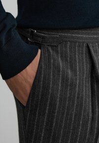 Gray pinstriped trousers in a wool blend, featuring a flat front, side pocket, and a dark sweater with ribbed cuffs. Adjustable waistband detail visible.