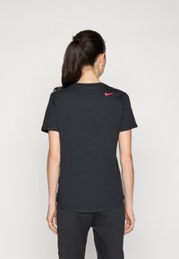 Svart bomull T-skjorte med korte ermer, rund hals, og rød Nike-logo på øvre rygg. Glatt tekstur, uformelt design.