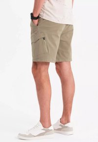 Shorts cargo beige avec une poche latérale, fabriqués en tissu léger. Associés à des baskets blanches et grises, avec un design à lacets.