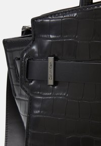 Černá kabelka z umělé kůže s texturou krokodýlí kůže, strukturovaným tvarem a výrazným stříbrným logem Calvin Klein.