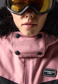 Rosa vanntett jakke med svarte detaljer, med pelskrage, store svarte knapper og et "even&odd ACTIVE" logo-patch.