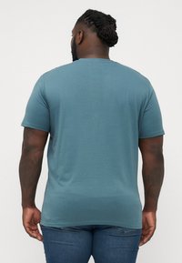 Short-sleeve, crewneck t-shirt in muted blue fabric. Smooth texture with a relaxed fit, featuring subtle stitching and a plain back design.