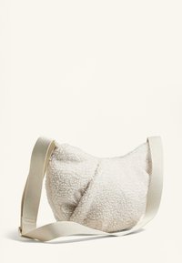 Borsa a tracolla in peluche bianco realizzata in soffice pile, caratterizzata da una forma curva e una tracolla regolabile beige. Design semplice senza accessori visibili.
