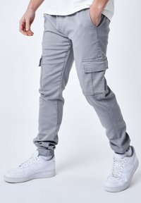 Pantalones cargo grises con bolsillos laterales, puños elásticos y una textura suave, combinados con zapatillas blancas. Diseño casual adecuado para ropa activa.