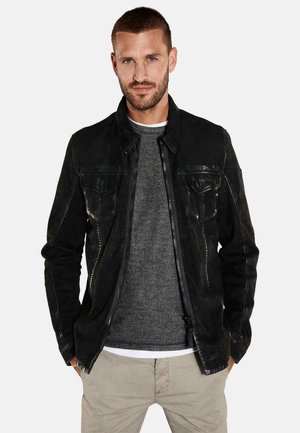 Black leather jacket with a zipper and button closure, featuring two chest pockets and a smooth texture. Worn over a gray sweater.