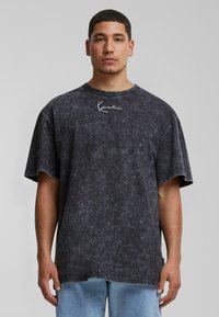 Short-sleeve, oversized black T-shirt with a faded texture and white embroidered logo on the chest. Cotton material, crew neck design.