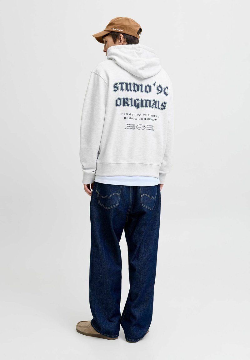 Sudadera gris con un gran estampado gráfico en la parte trasera, combinada con jeans de corte suelto en azul oscuro y calzado claro, sobre un fondo simple.