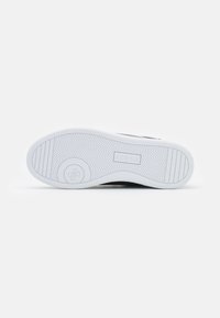 Suola di sneaker nera con suola in gomma bianca che presenta un motivo a spina di pesce, logo impresso e dettagli testurizzati lungo i bordi.