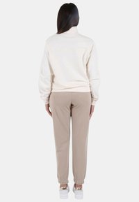 Felpa color crema con collo alto, abbinata a pantaloni jogger beige. Tessuto morbido, polsini elasticizzati e sneakers bianche con dettagli dorati.