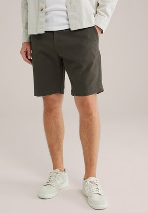 Olive green shorts made from cotton blend fabric, featuring a structured design, side pockets, and a regular fit, paired with white sneakers.