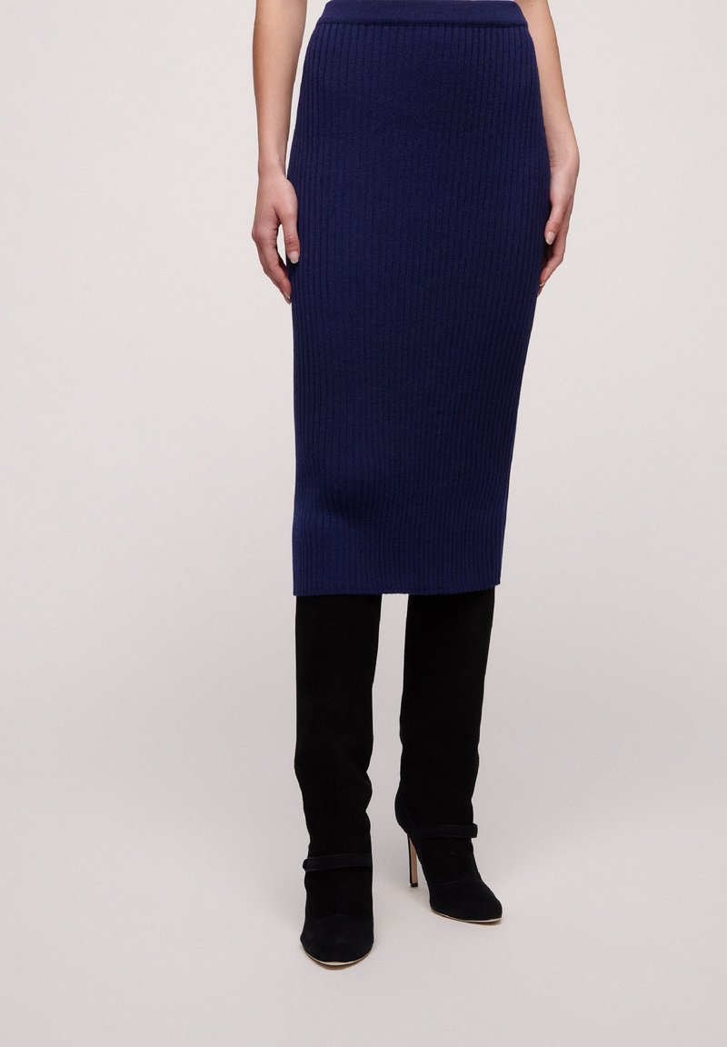 Ribbed navy knit midi skirt, fitted design. Paired with tall black suede heeled boots featuring a double-layer accent strap at the ankle.