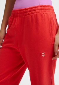 Rode sweatpants met een elastische tailleband, voorzien van een klein wit chevronlogo aan de linkerkant, gemaakt van zachte, comfortabele stof.