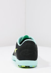 Czarny but sportowy z fakturowaną cholewką, miętowozielonymi akcentami, wyściełanym kołnierzem oraz kontrastową podeszwą z jasnymi żółtymi i czarnymi wzorami.