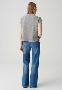 Un haut tricoté gris à manches courtes, affichant un motif texturé, associé à un jean flare bleu taille haute avec des poches arrière.