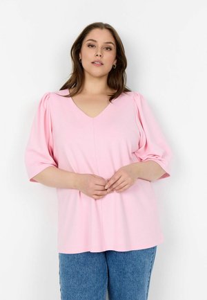 Różowa bluzka z dekoltem w serek i krótkimi bufkami, wykonana z miękkiego materiału. W połączeniu z niebieskimi dżinsami o luźnym kroju i prostym designie.