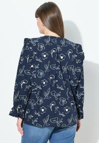 Blusa navy con pattern floreale bianco, spalle arruffate e maniche lunghe. Tessuto morbido, presenta una piega sul retro e polsini arricciati.