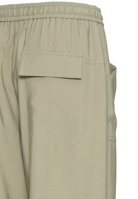 Pantalon cargo beige clair avec une taille à cordon de serrage, doté d'une poche arrière plate et d'une poche sur la couture latérale, fabriqué en tissu résistant avec des coutures visibles.