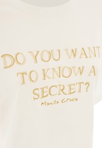 T-shirt en coton blanc avec un col rond, arborant un texte brodé en or : "VEUX-TU CONNAÎTRE UN SECRET ? Manila Grace."