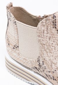 Scarpa slip-on beige con texture in pelle di serpente, pannelli laterali elastici intrecciati e una suola bianca spessa con strisce marroni.