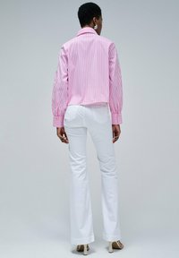 Chemise cropped à rayures roses et blanches avec des manches bouffantes, des poignets boutonnés et de la broderie florale sur les manches. Associée à un pantalon flared blanc.