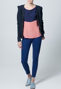 Námořnický a růžový top se střihem bloků barev, navy svetr na zip, modré slim-fit kalhoty, světle modré boty se stříbrnými detaily.