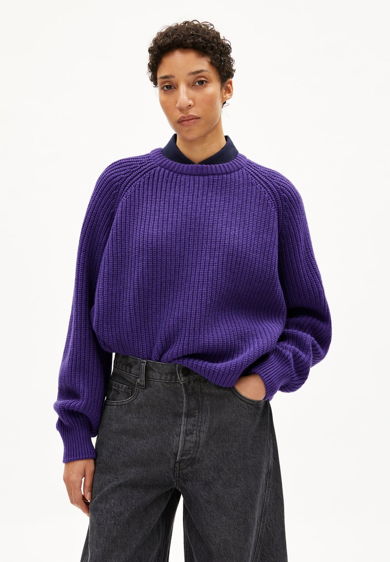 Lila geripptes Strickpullover mit Rundhalsausschnitt, langen Ärmeln und lockerer Passform, kombiniert mit hochtaillierten schwarzen Jeans.