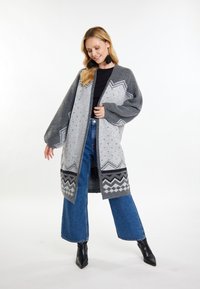 Cardigan a maglia grigia e grigio chiaro con un motivo, con maniche larghe, che presenta disegni geometrici e colletto scialle, abbinato a pantaloni in denim scuro.