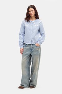 Blå og hvit stripete skjorte med knapper og stor hvit blondekrage, kombinert med falmede, løstsittende jeans og brune lærsko.