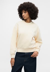 Φούτερ σε εκρού απόχρωση με στρογγυλή λαιμόκοψη και ριμπ μανσέτες, με διακριτικό λογότυπο. Συνδυασμένο με σκούρο τζιν παντελόνι. Ομαλή υφή.