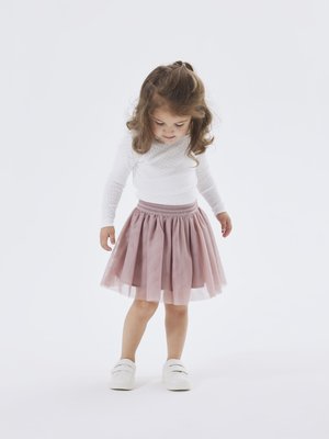 Gonna in tulle rosa chiaro con vita arricciata, abbinata a un top bianco a maniche lunghe con texture a pois e sneakers bianche.