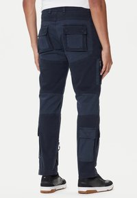 Pantaloni cargo blu navy con multiple tasche, vestibilità dritta, textures a contrasto e cerniere sui lati. Design casual con un tessuto resistente.