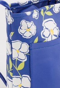 Bolso azul con un patrón floral de flores blancas y hojas verdes, fabricado en material sintético texturizado. Incluye un bolsillo lateral.