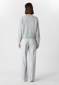Jasnoszary, puszysty sweter z długimi rękawami i ściągaczem na dole, w zestawie z jasnoszarymi, szerokimi spodniami. Model odwrócony tyłem, minimalistyczny design.