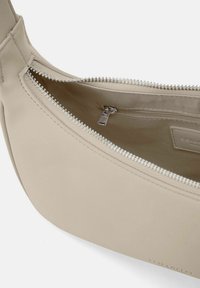 Borsa a tracolla beige con un esterno in finta pelle liscia, tasca con zip e una morbida fodera in tessuto che presenta un comparto interno con zip.