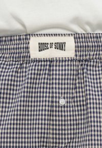 Μπλε και κρεμ σορτς με καρό μοτίβο γκίνχαμ και ελαστική μέση. Διαθέτει λευκή ετικέτα με την ένδειξη "HOUSE OF SUNNY" και ένα μόνο κουμπί.