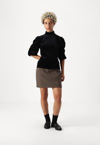 Fekete bársony felső, puffos ujjakkal és magas nyakkal, barna és krémszínű houndstooth mini szoknyával és fekete loaferekkel párosítva.