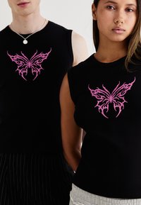Black ribbed tank tops feature a prominent pink butterfly design on the chest. The tops are sleeveless and fitted, showcasing a minimalist style.