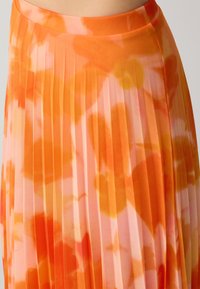 Faltenrock in Orange- und Rosatönen mit floralem Muster. Hergestellt aus leichtem Stoff, mit glatter Textur und fließendem Design.