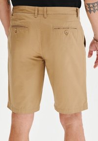 Khaaki szorty wykonane z mieszanki bawełny, z prostym krojem, dwoma tylnymi kieszeniami z zapięciem na guziki oraz przeszywanym dołem.
