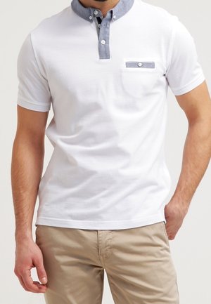 White polo shirt with a gray collar, button placket, and a chest pocket. Short sleeves and a fitted design. Cotton material.